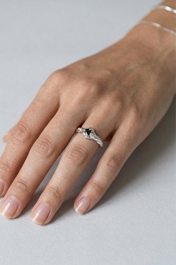 Hand wearing a silver ring with a black gemstone on a light gray background