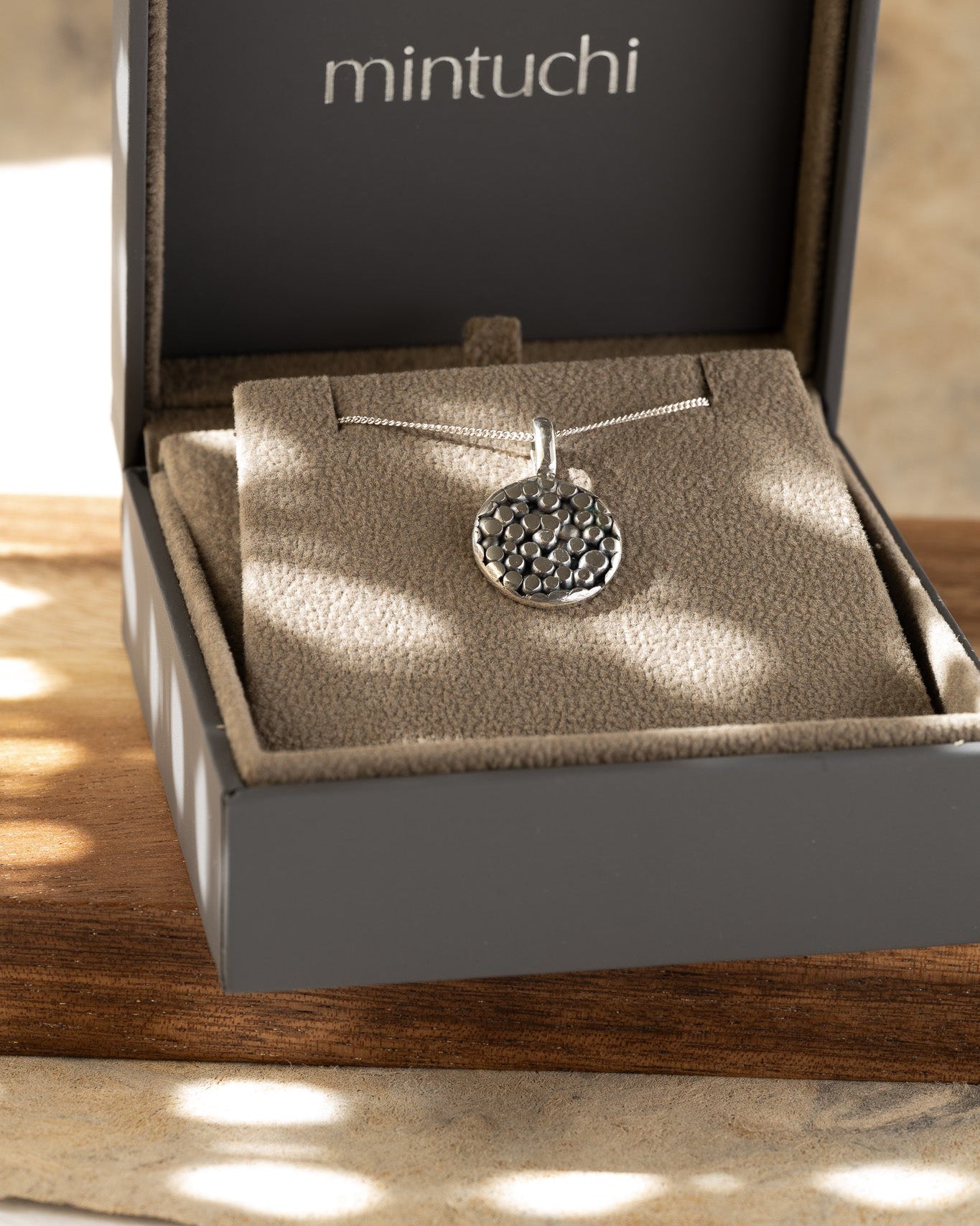 Silver necklace with a pendant in an open jewelry box labeled 'mintuchi'.