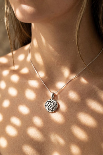 Necklace with a textured pendant on a person's neck, casting shadows on the skin.