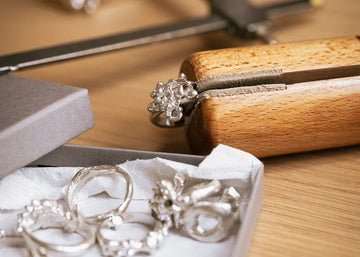 Silver jewelry on a wooden table with tools and a box.