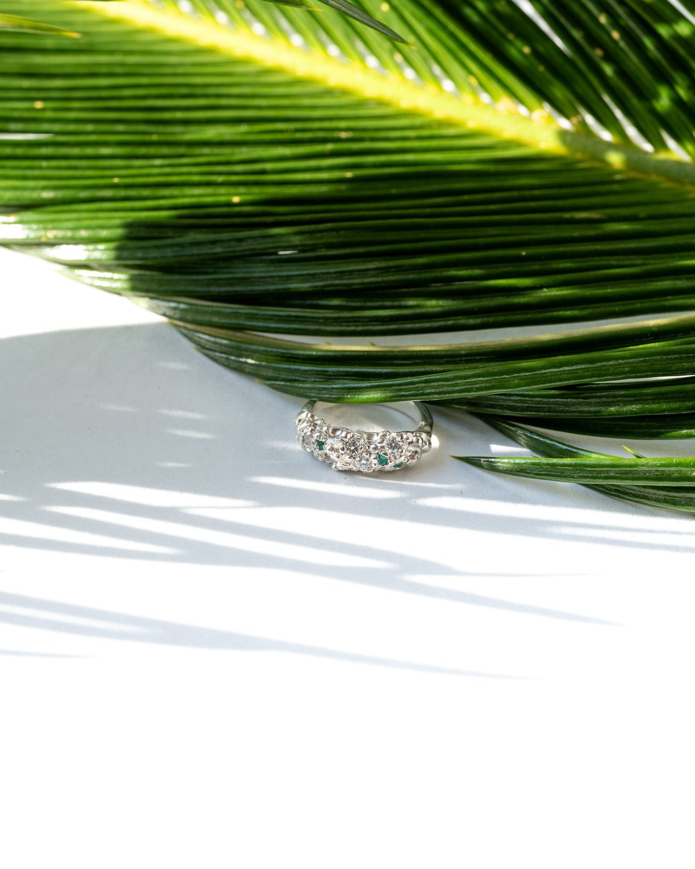 Silver ring with green gemstones on a white surface with palm leaf