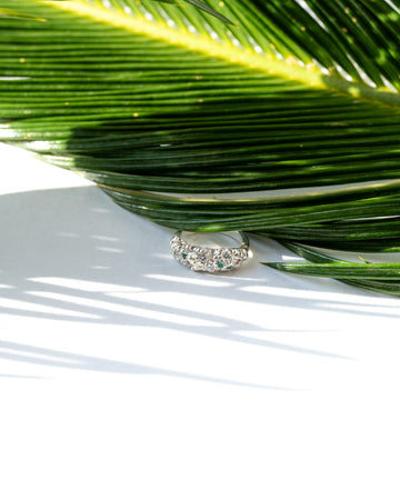 Silver ring with green gemstones on a white surface with palm leaf