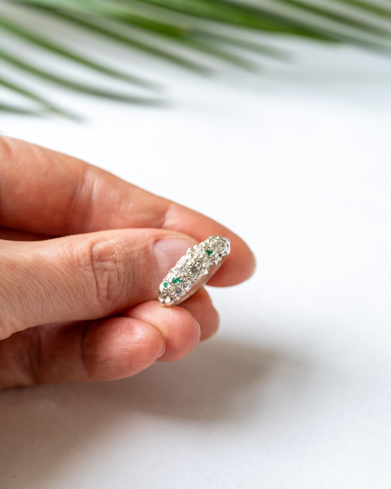 Hand holding a ring with green gemstones against a white background