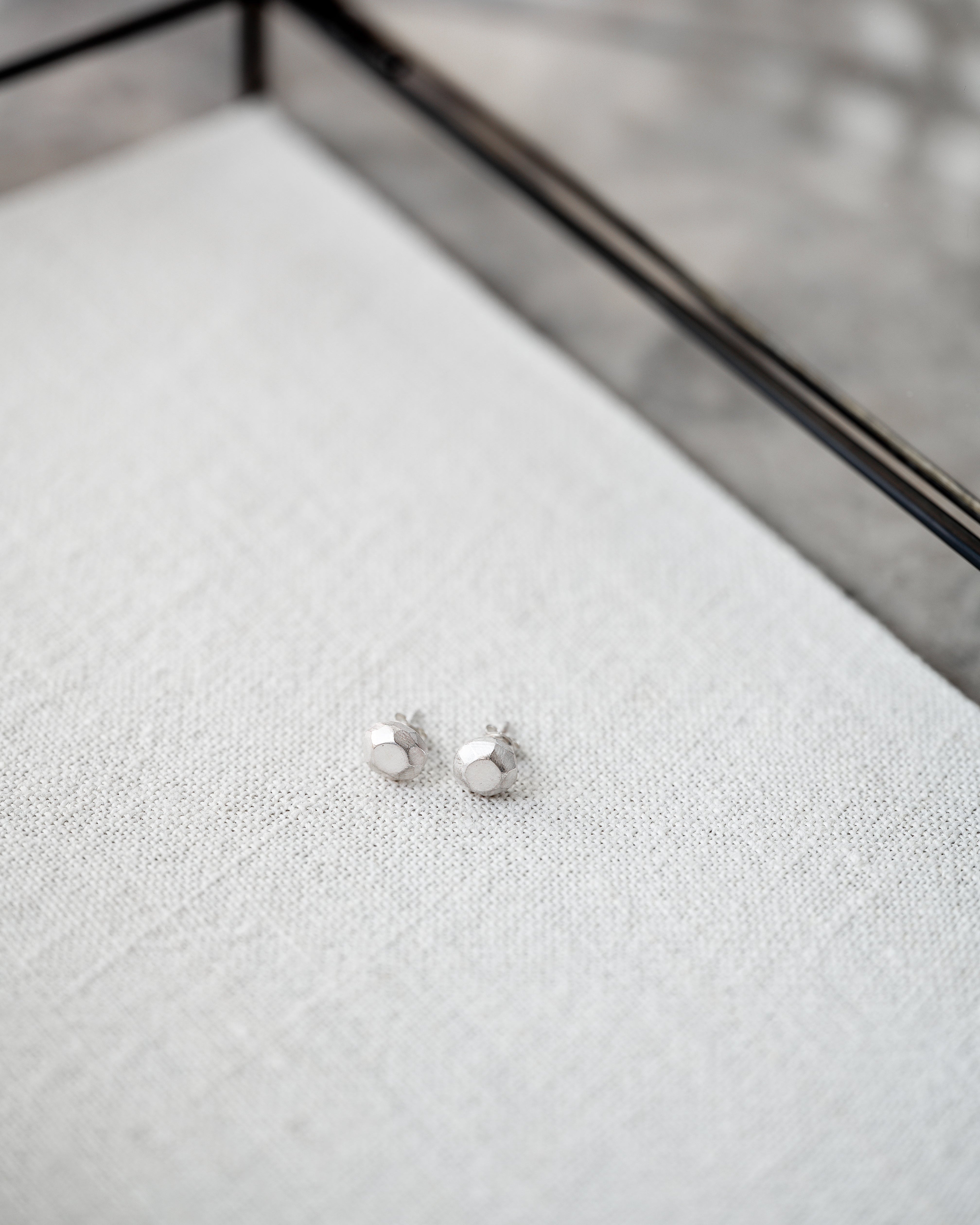 Silver stud earrings on a textured white surface with a geometric black frame in the background.