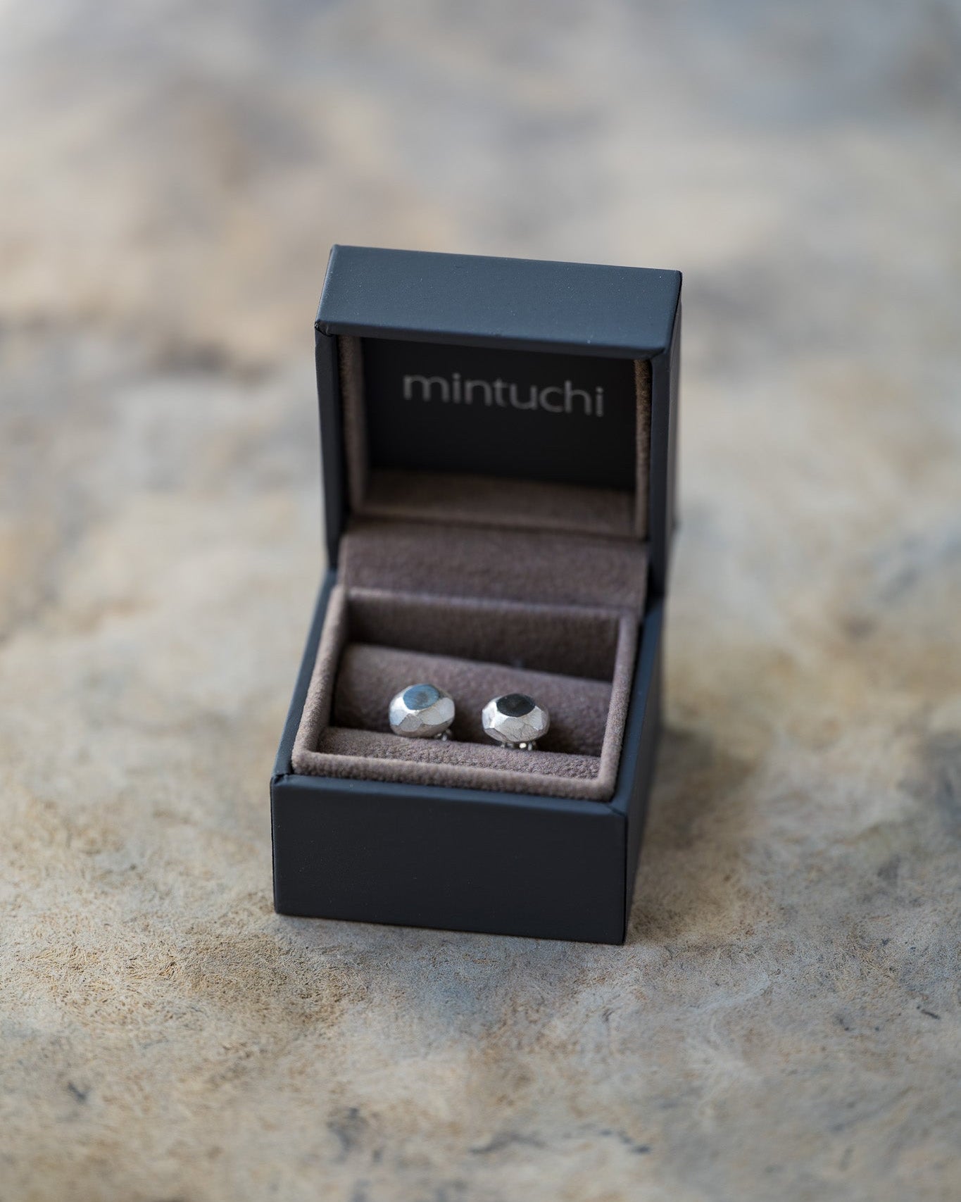 Pair of earrings in a black 'mintuchi' box on a stone surface