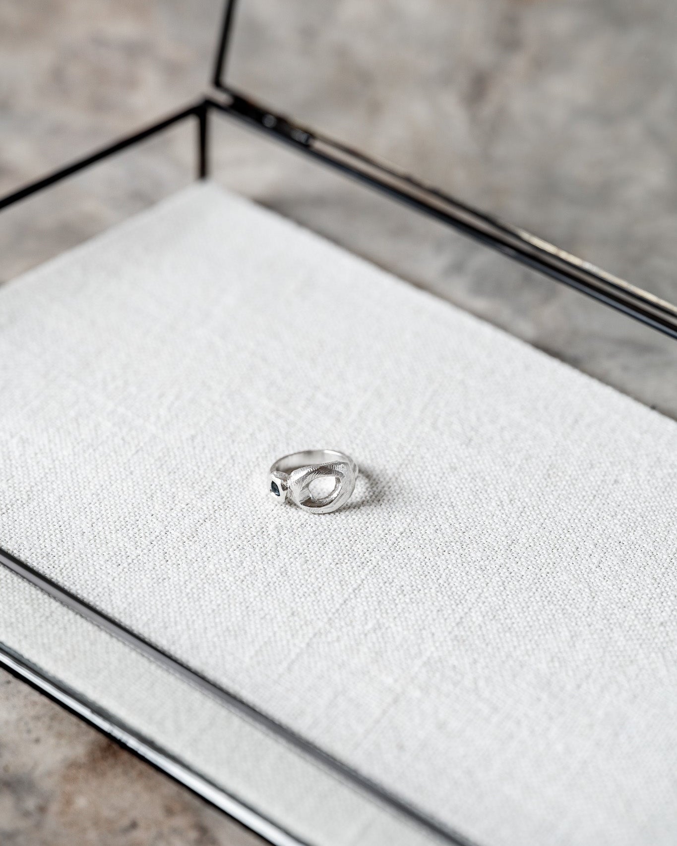 Silver ring on a textured white surface inside a jewelry box with a neutral background