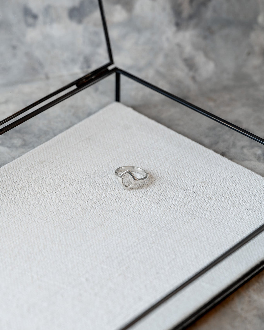 Silver ring in a glass display case on a textured surface