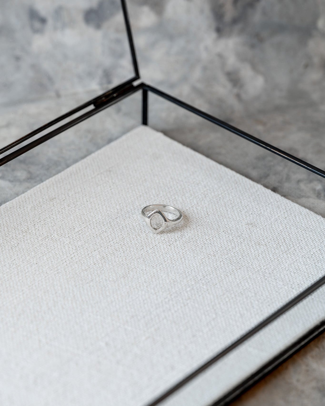 Silver ring in a glass display case on a textured surface