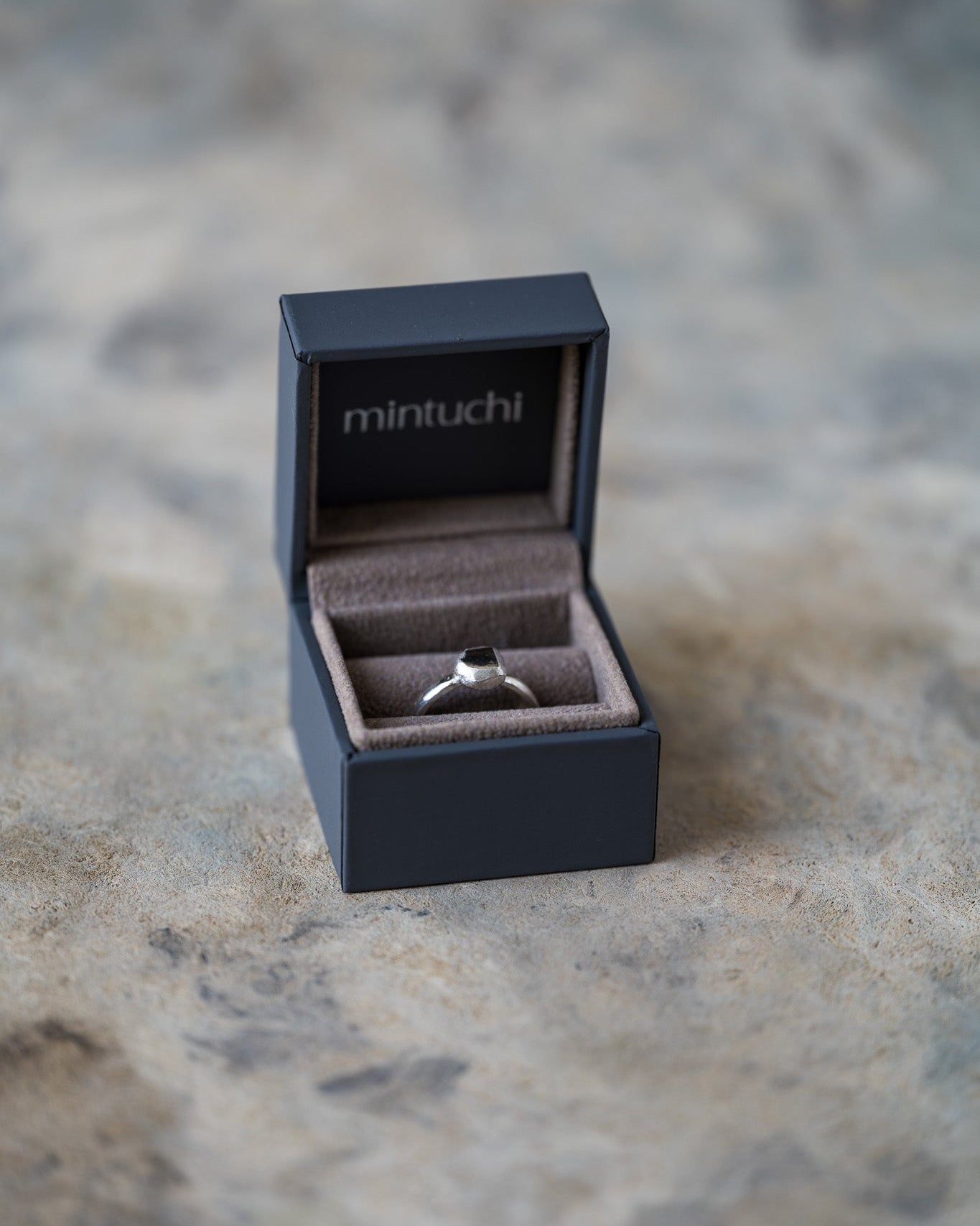 Silver ring in a 'mintuchi' box on a textured surface
