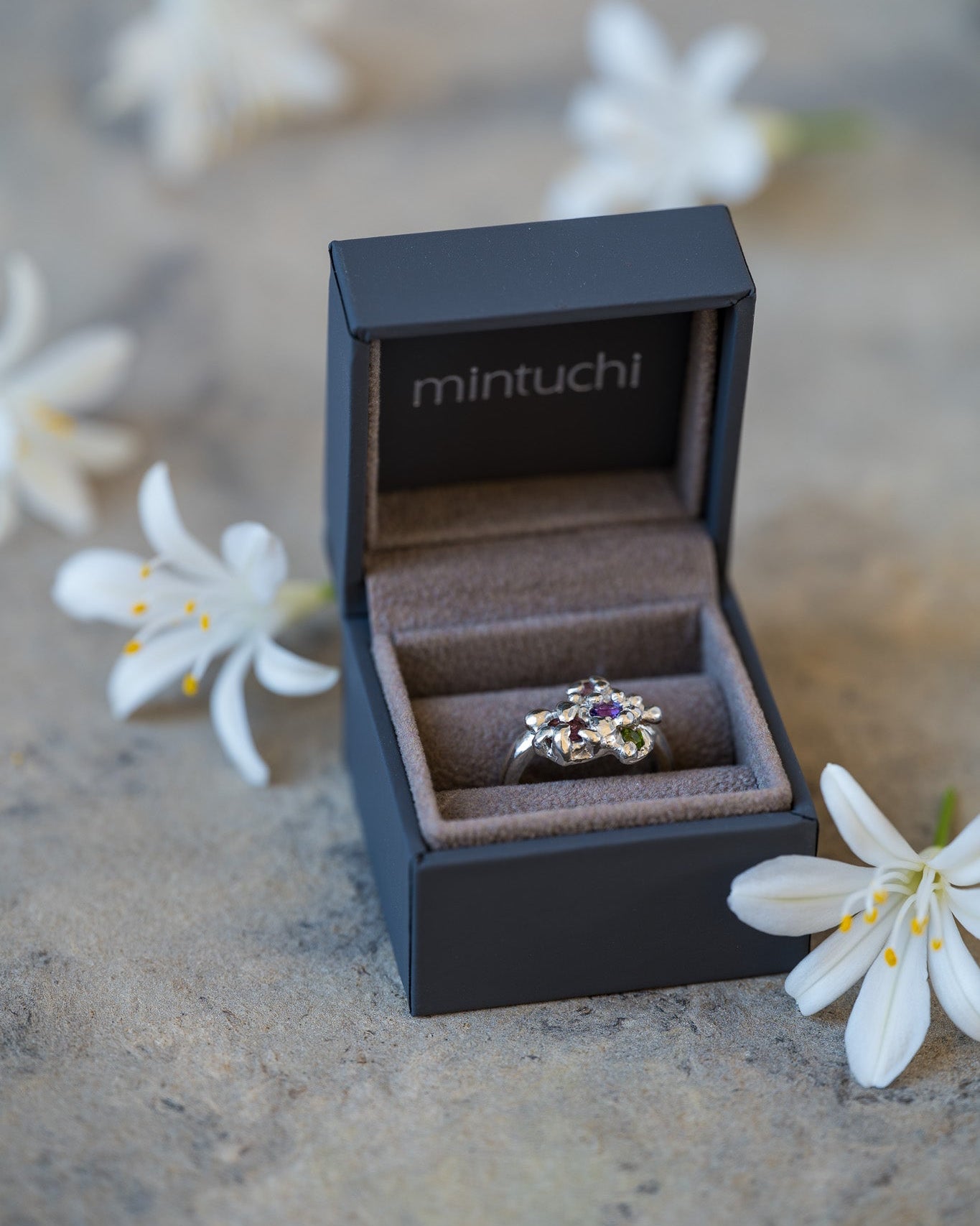 Ring in a 'mintuchi' box with white flowers on a stone surface