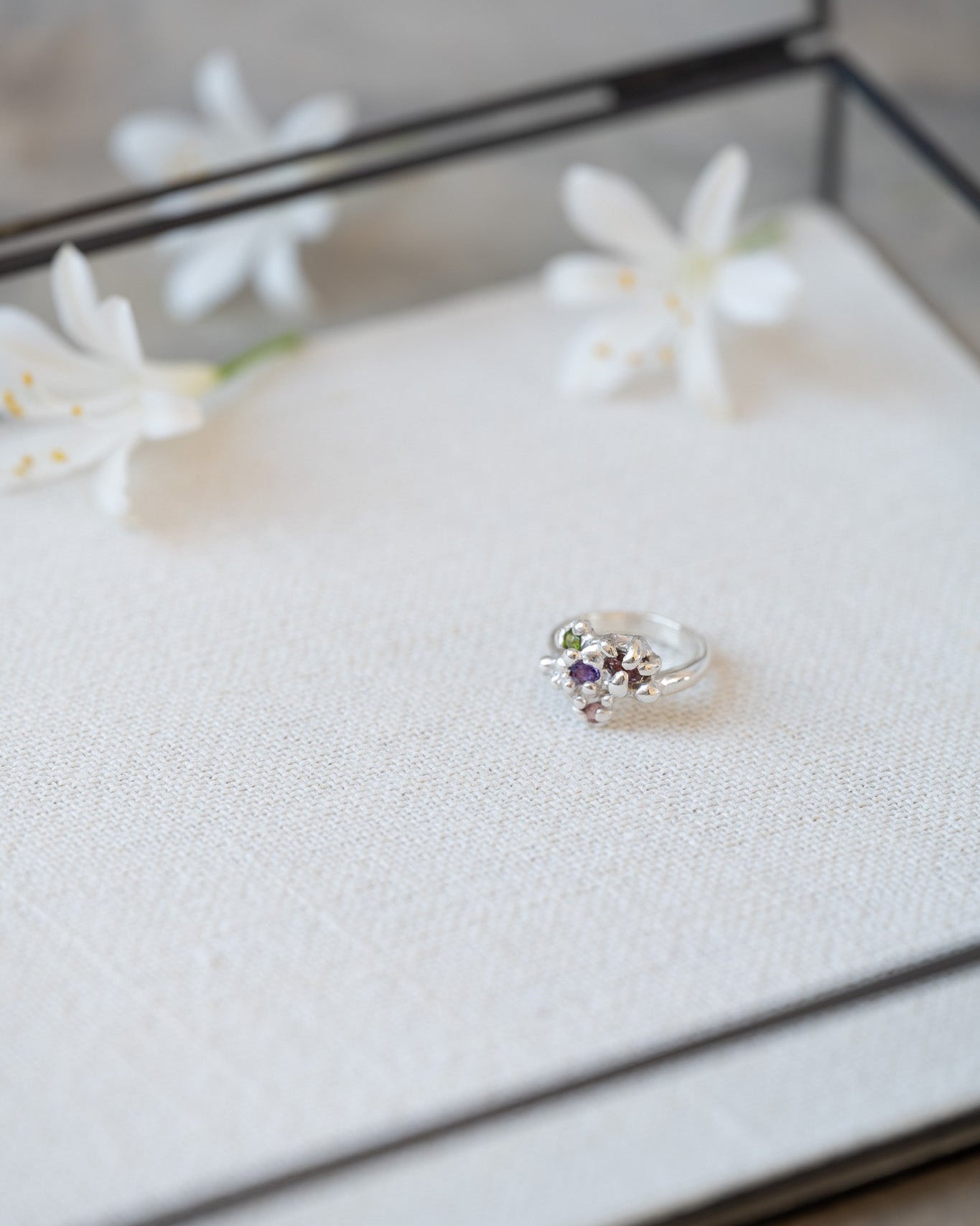 Silver ring with gemstones in a jewelry box with white flowers