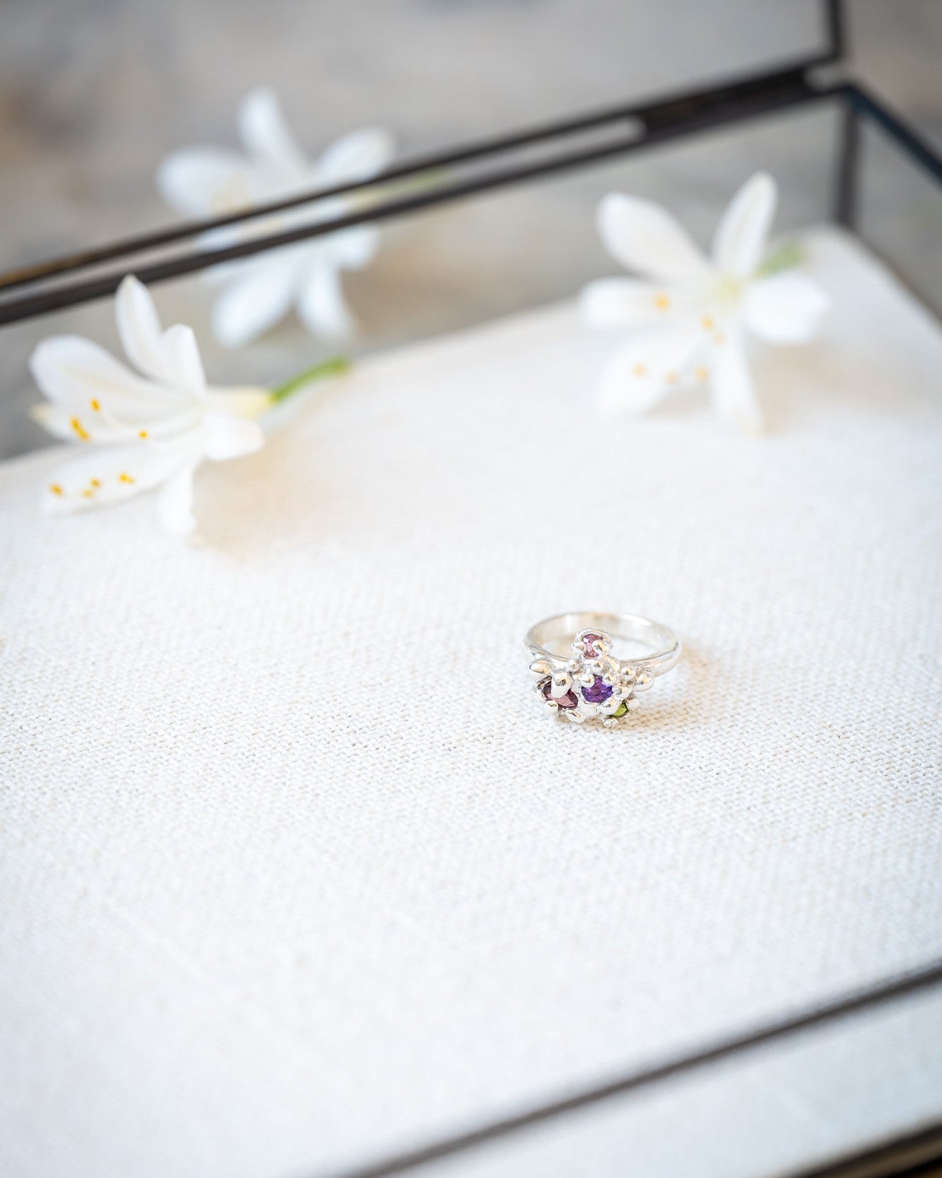 Jewelry box with a ring featuring a purple gemstone and white flowers on top.
