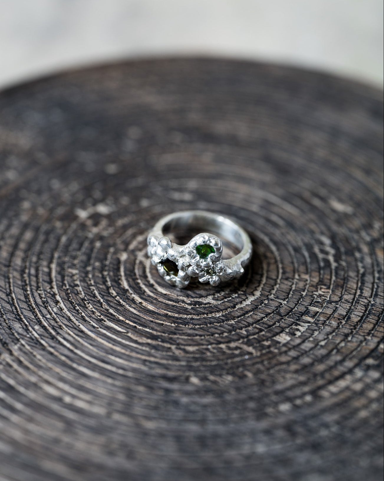 Silver ring with green gemstone on a textured wooden surface