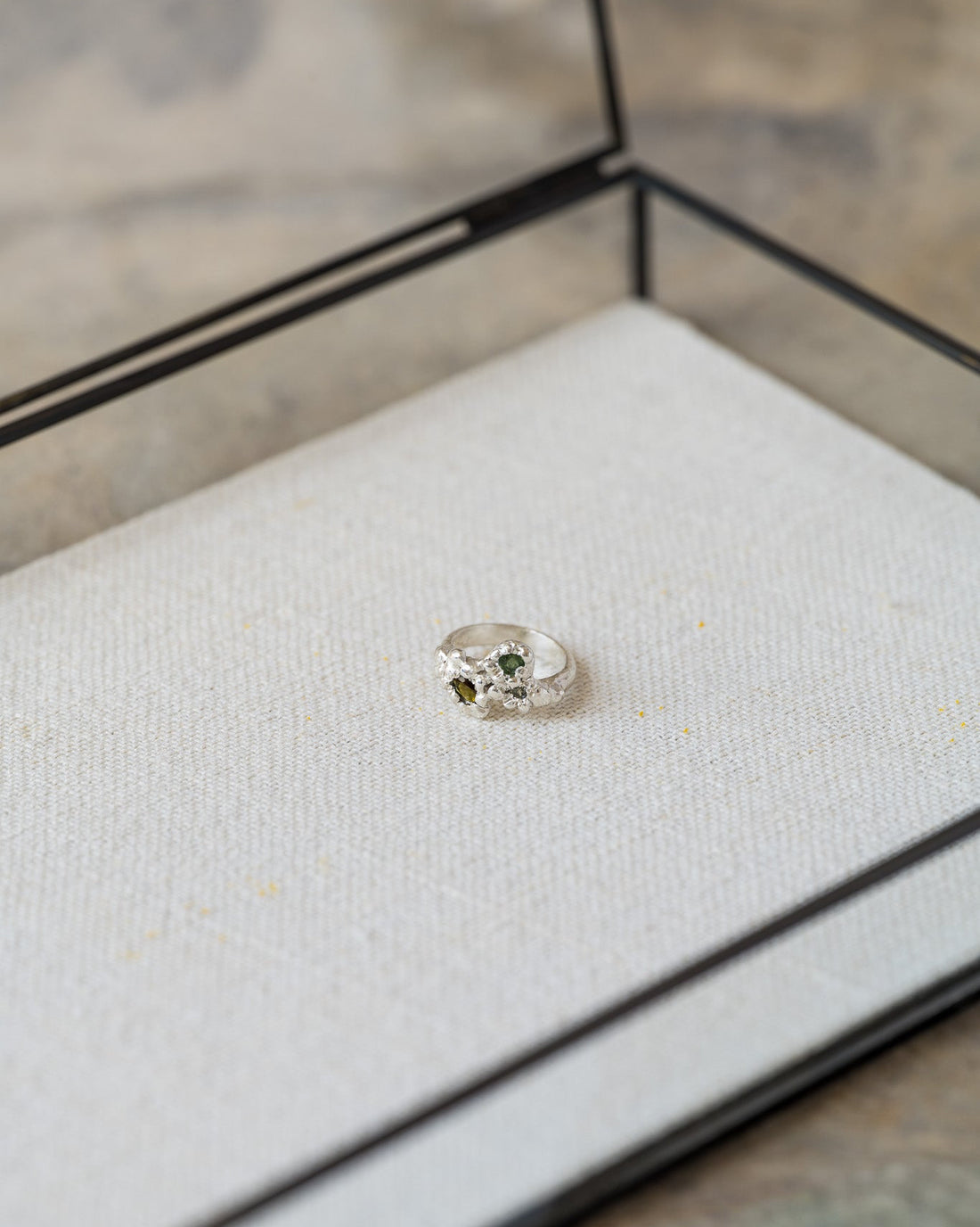 Ring with green gemstone in a wooden box on a textured surface