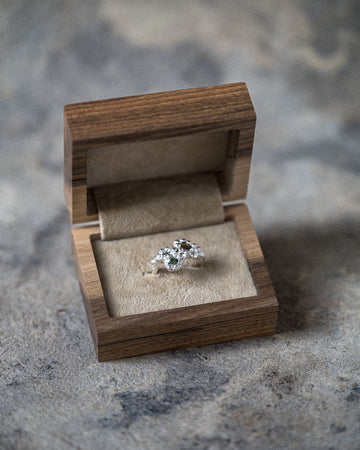Ring with green gemstone in a wooden box on a textured surface