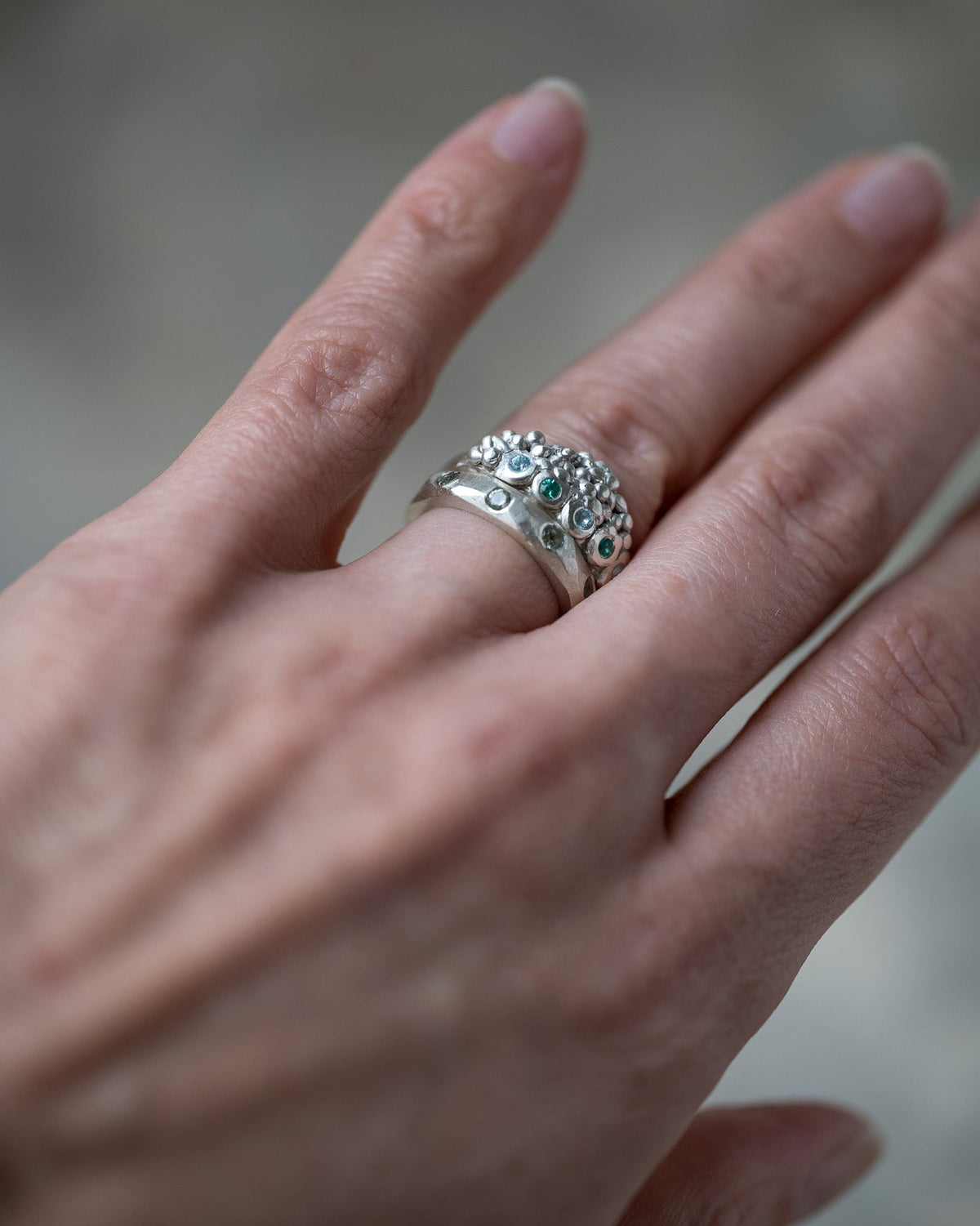 A close-up of a hand wearing a silver ring decorated with small round blue-green stones.