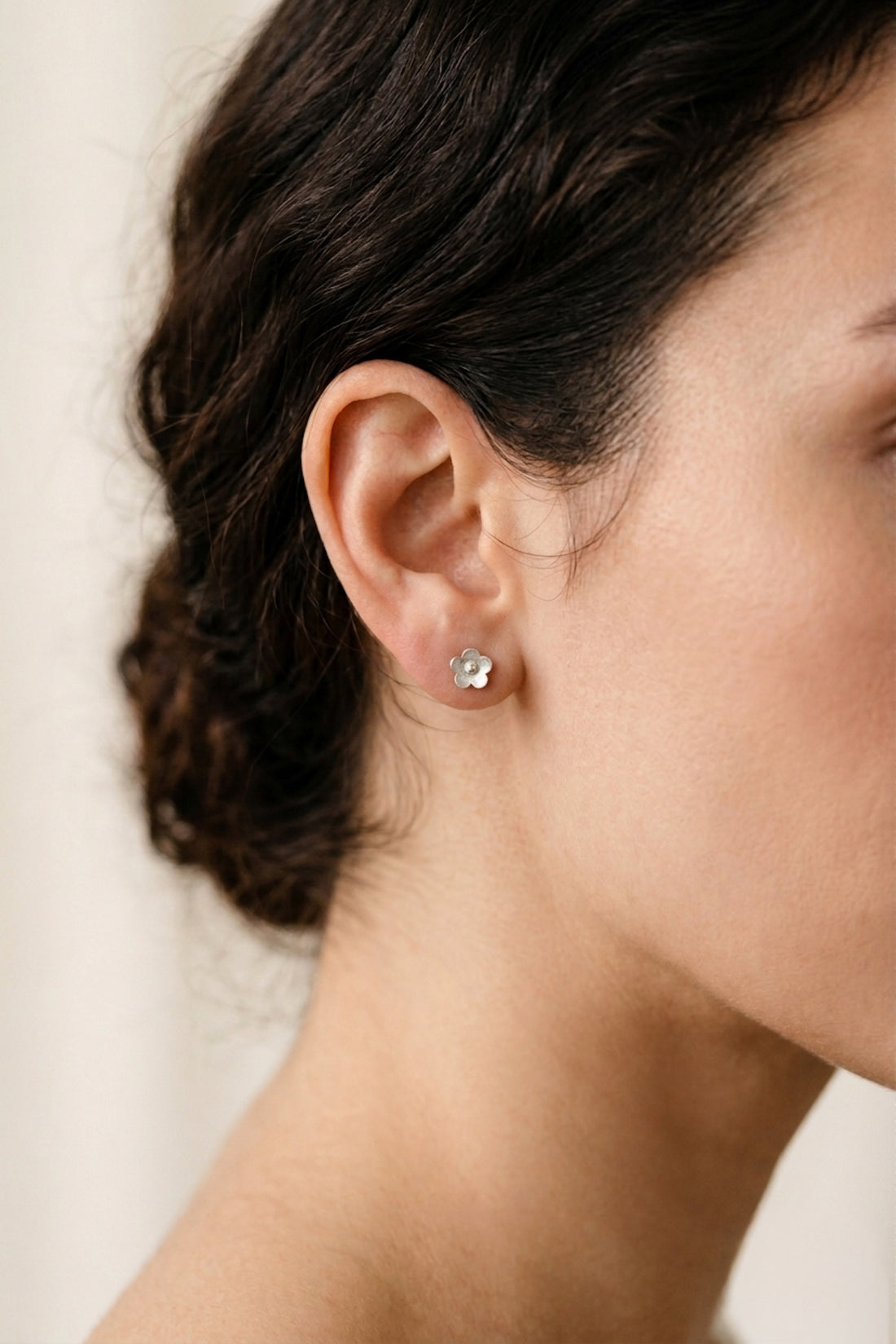 Close-up of a person wearing diamond stud earrings with a neutral background