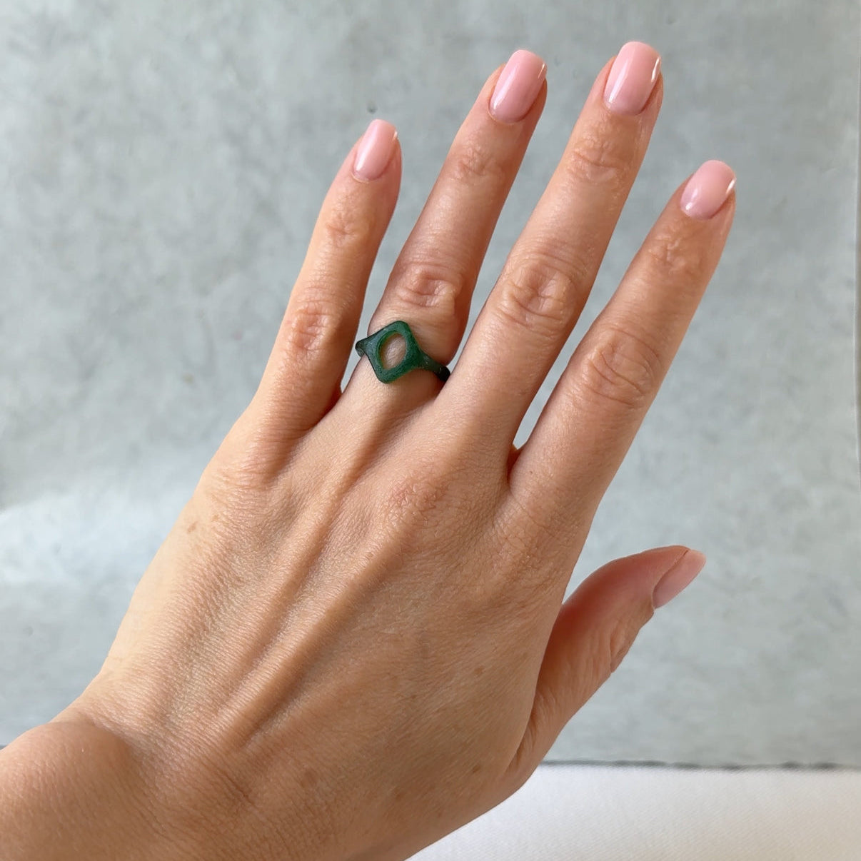 Hand wearing a green ring on a neutral background