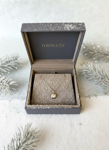 Necklace in a 'mintuchi' branded box on a textured surface with dried flowers.
