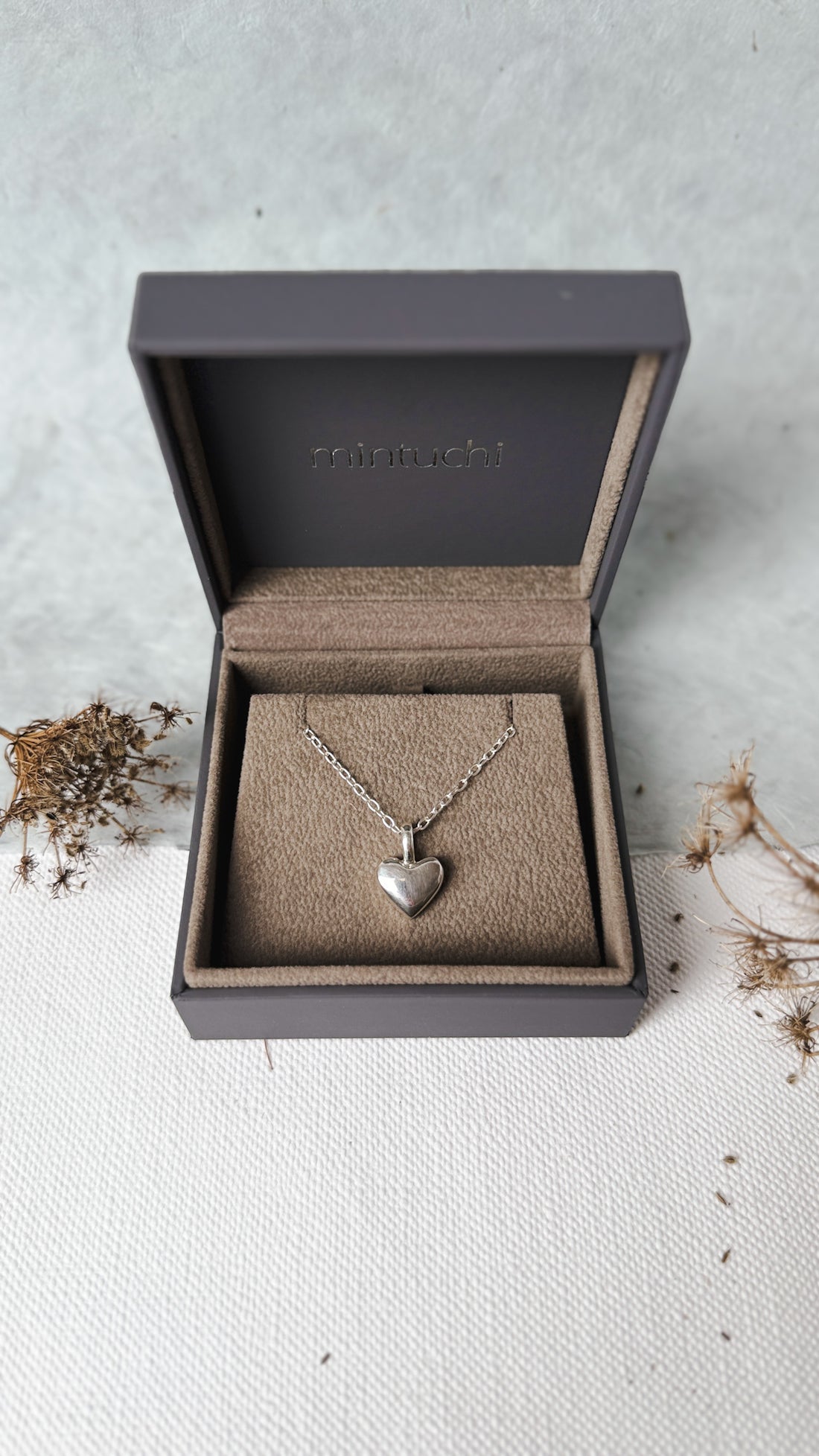 Silver heart necklace in an open jewelry box on a light surface