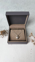 Silver heart necklace in an open jewelry box on a light surface