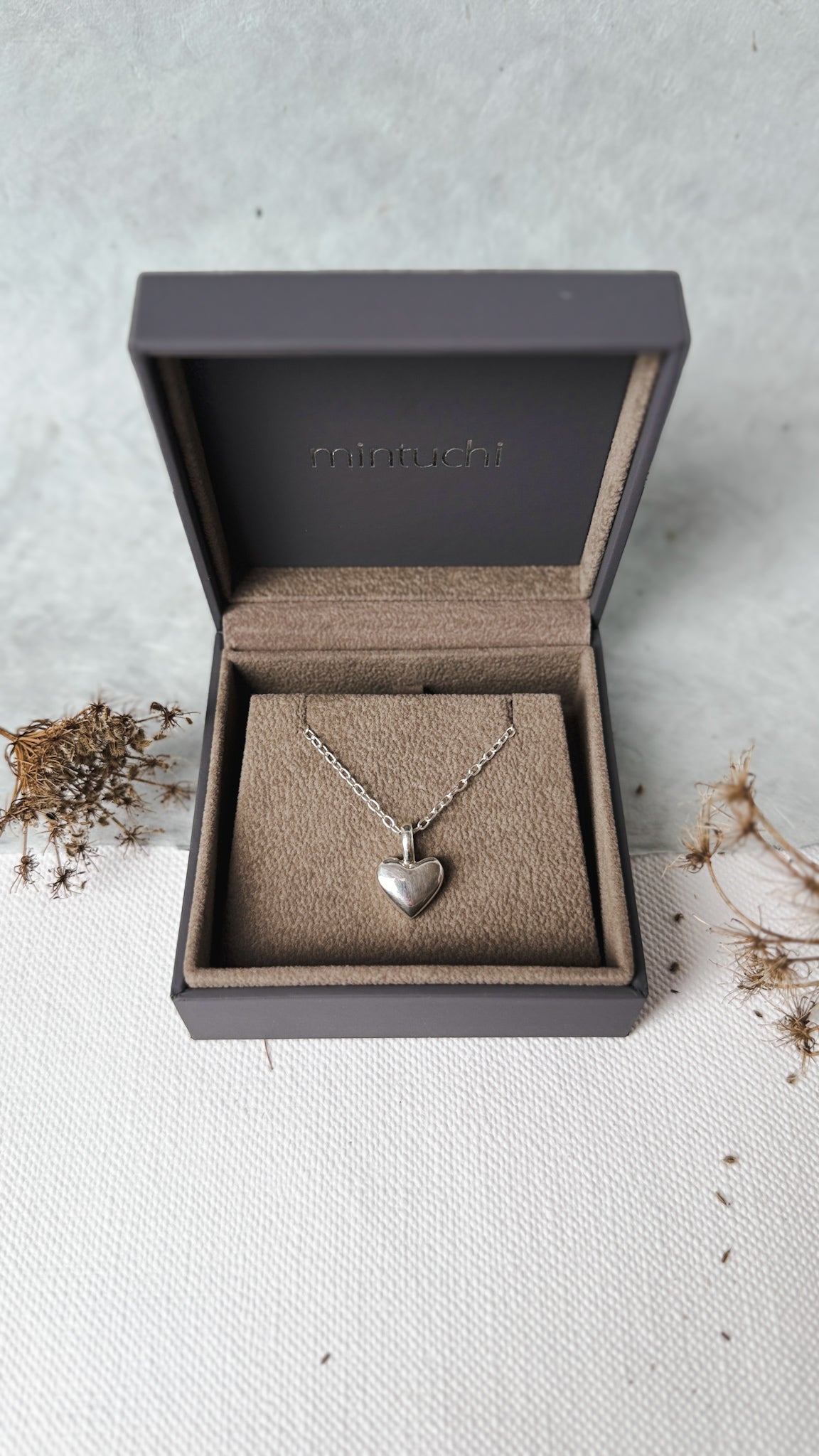 Silver heart necklace in an open jewelry box on a light surface