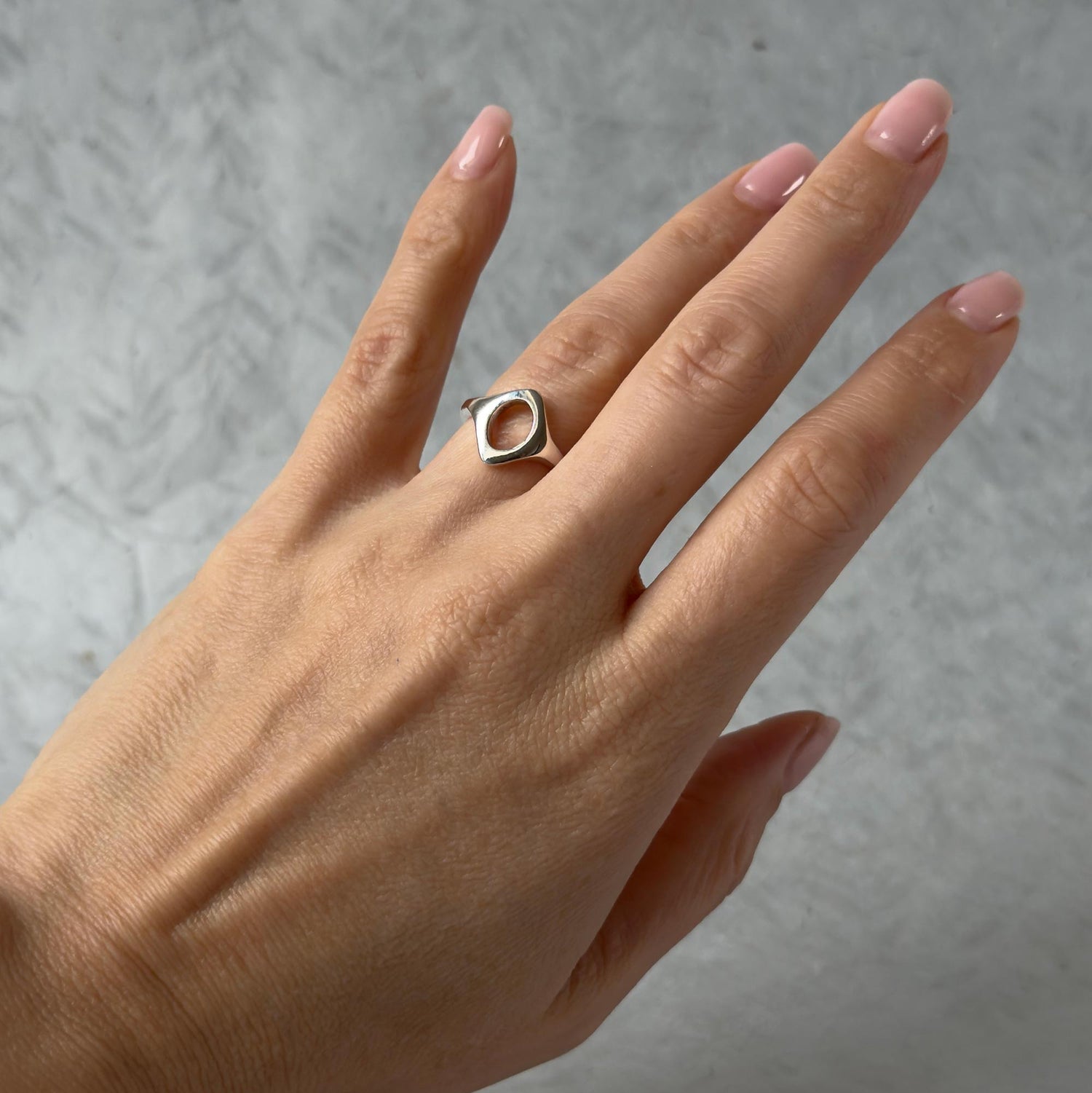 Hand wearing a silver ring with a geometric design on a gray background