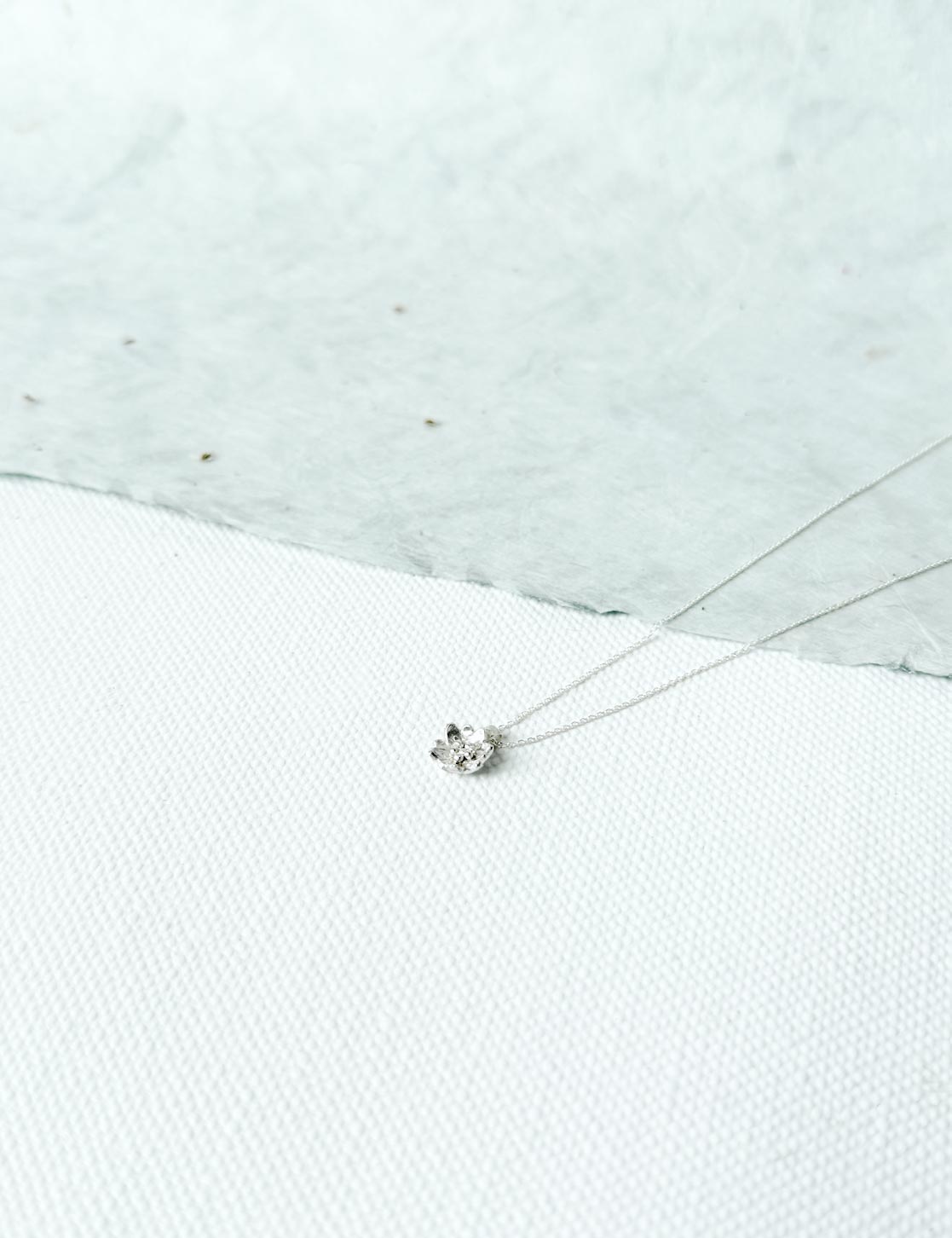Silver necklace with a pendant on a textured white surface