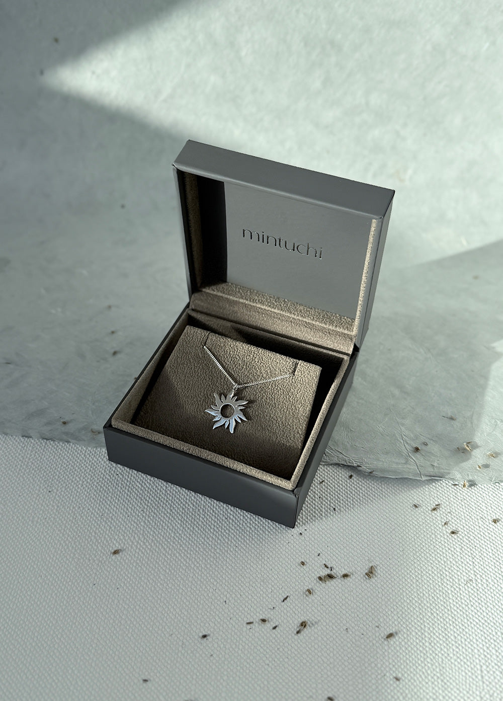 Silver necklace with a starflower pendant in a 'minucho' box on a textured surface.
