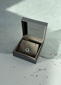 Silver necklace with a starflower pendant in a 'minucho' box on a textured surface.