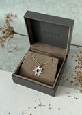 Sunflower necklace in a branded box on a textured surface with dried flowers.