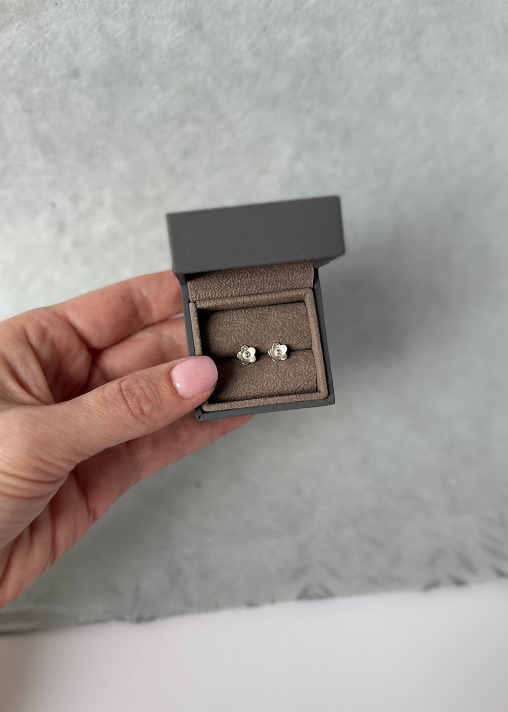 Close-up of a person wearing diamond stud earrings with a neutral background